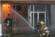 One fire fighter on the walkie talkie while two others spray a fire inside a building