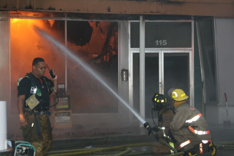 One fire fighter on the walkie talkie while two others spray a fire inside a building